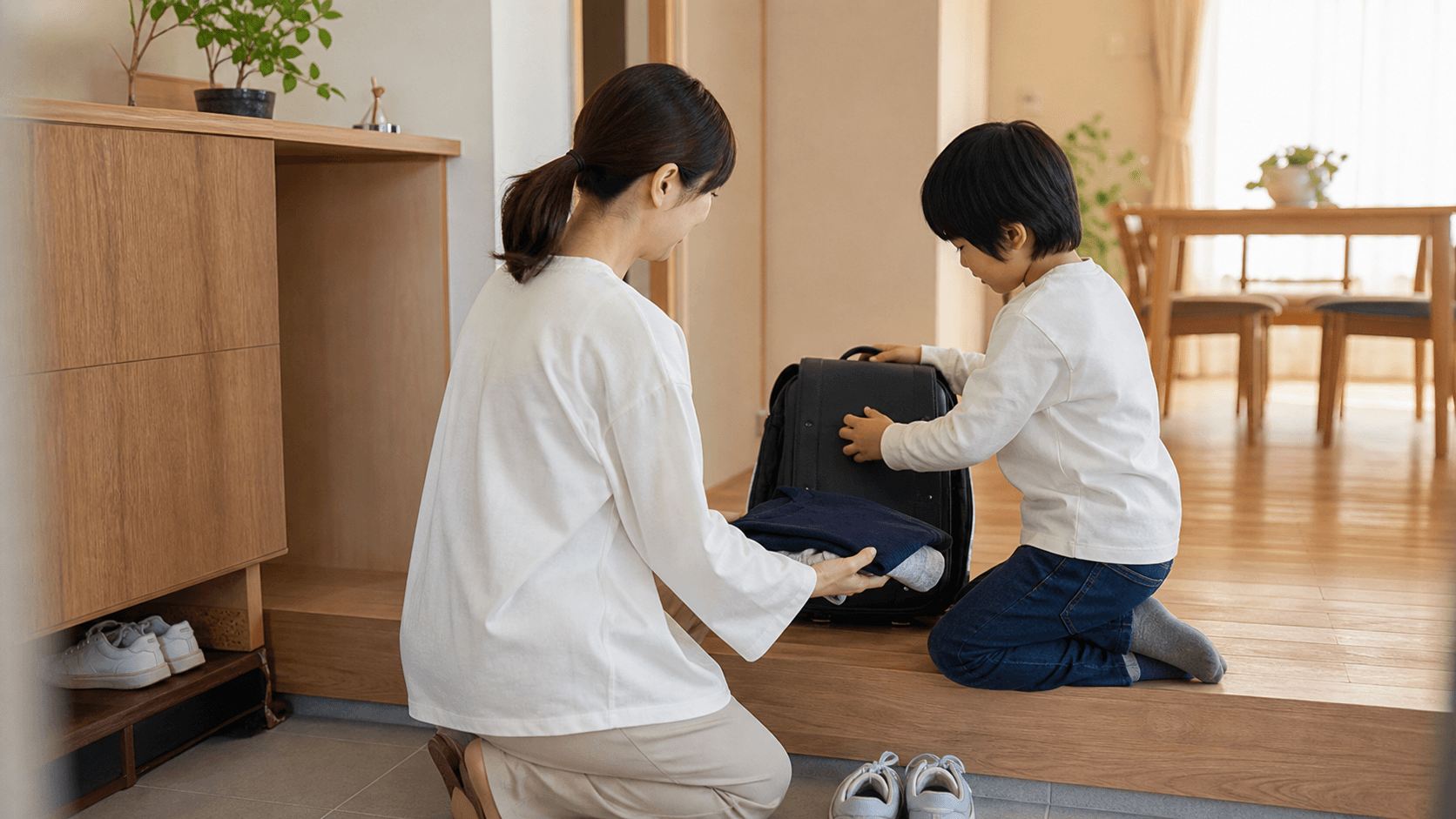 玄関で子どもが保護者と一緒に通学バッグを準備している場面