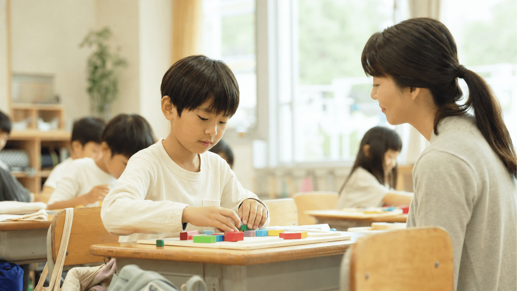 教室で子どもが机上の活動に取り組み支援者が見守っている場面