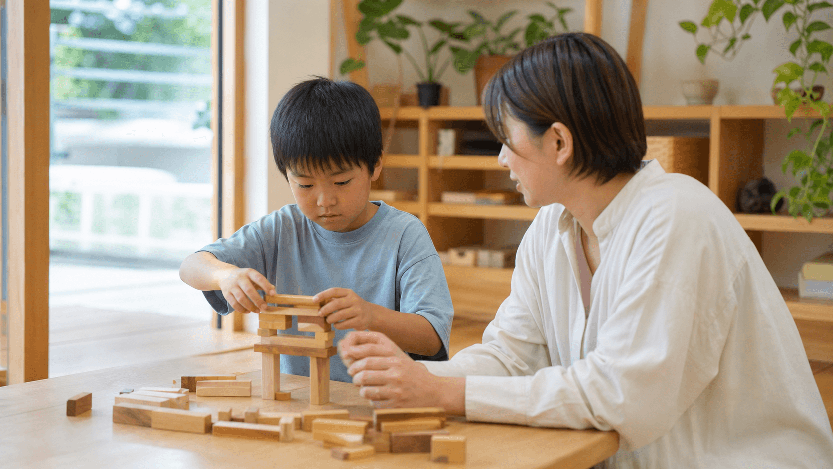 子どもが木のブロックで遊び支援員がそばで見守っている場面