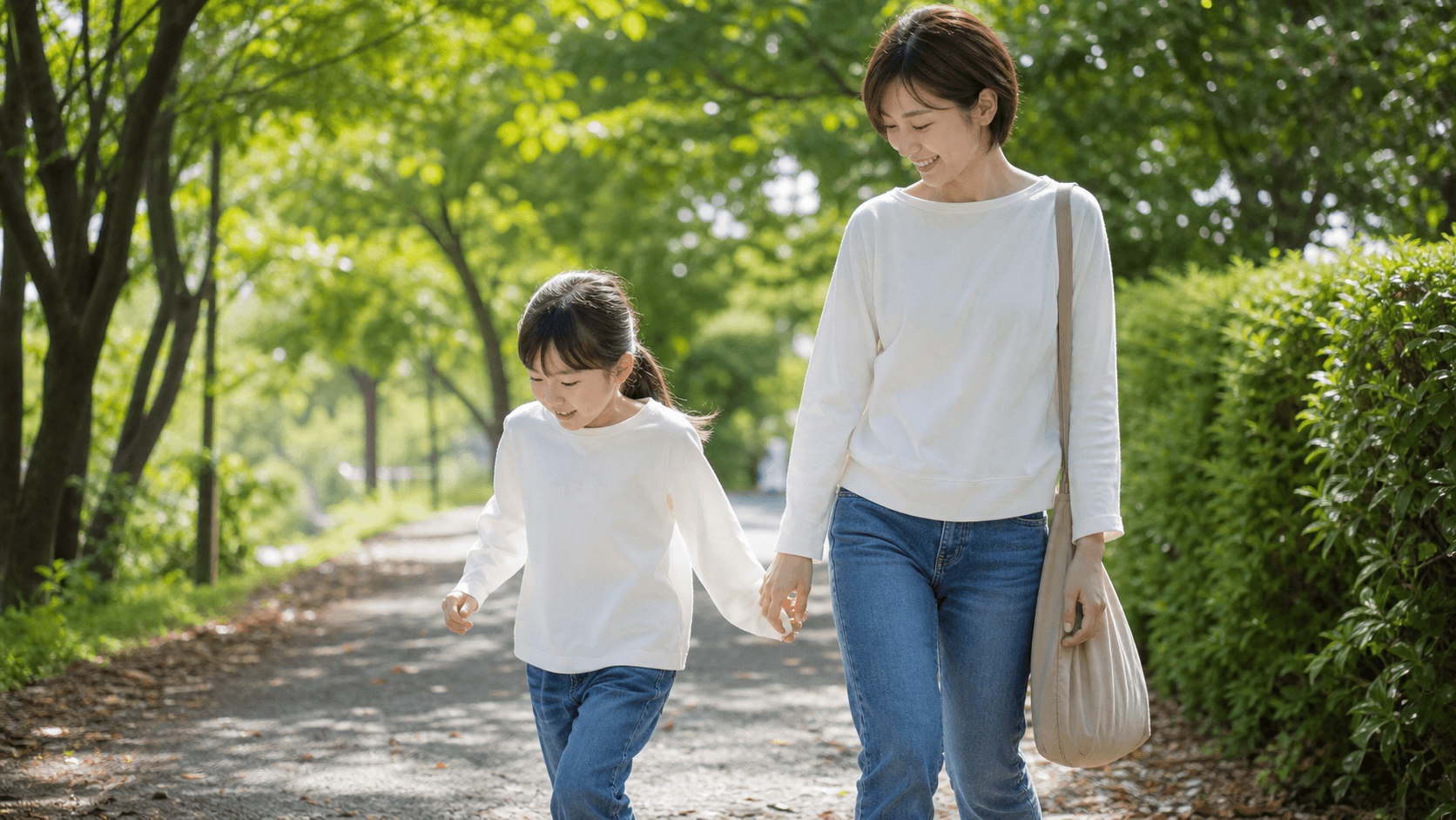緑の多い公園で保護者と子どもが手をつないで歩いている場面
