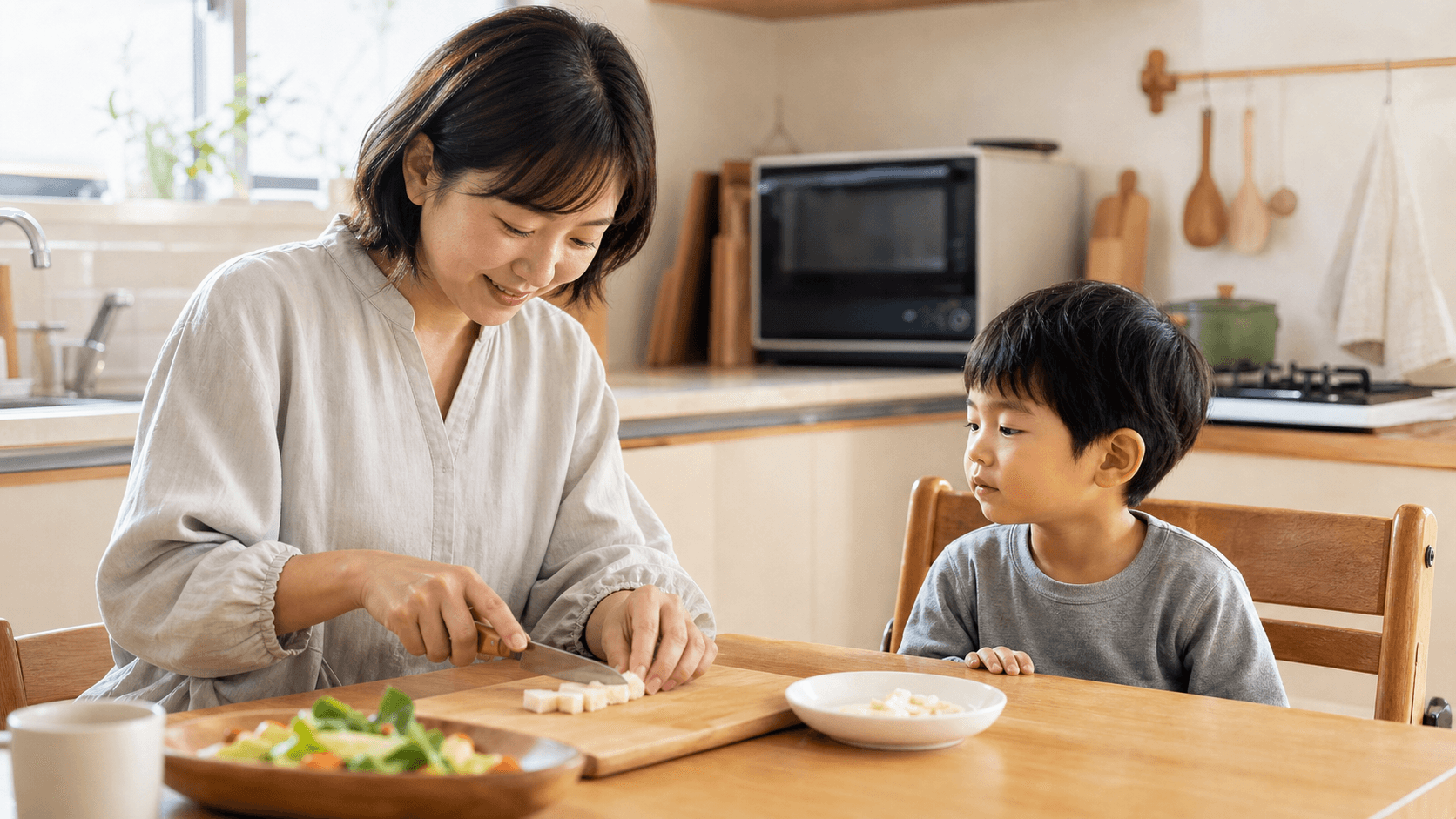保護者がキッチンで子どもの食べ物を小さく切っている場面