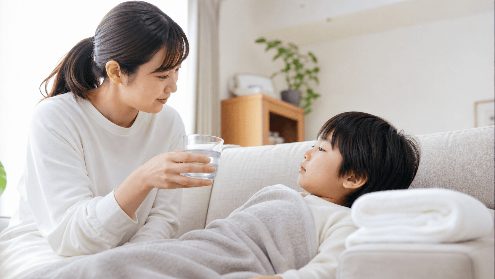 ソファで休む子どもに保護者が水を差し出している場面